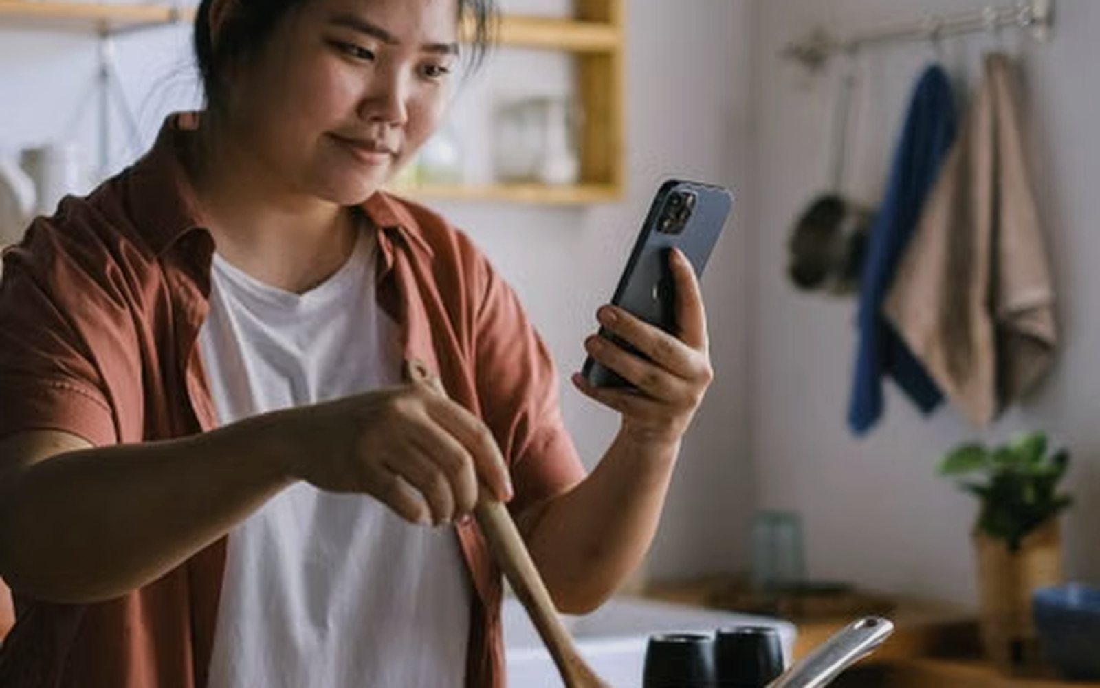 A woman cooking at home while checking her phone